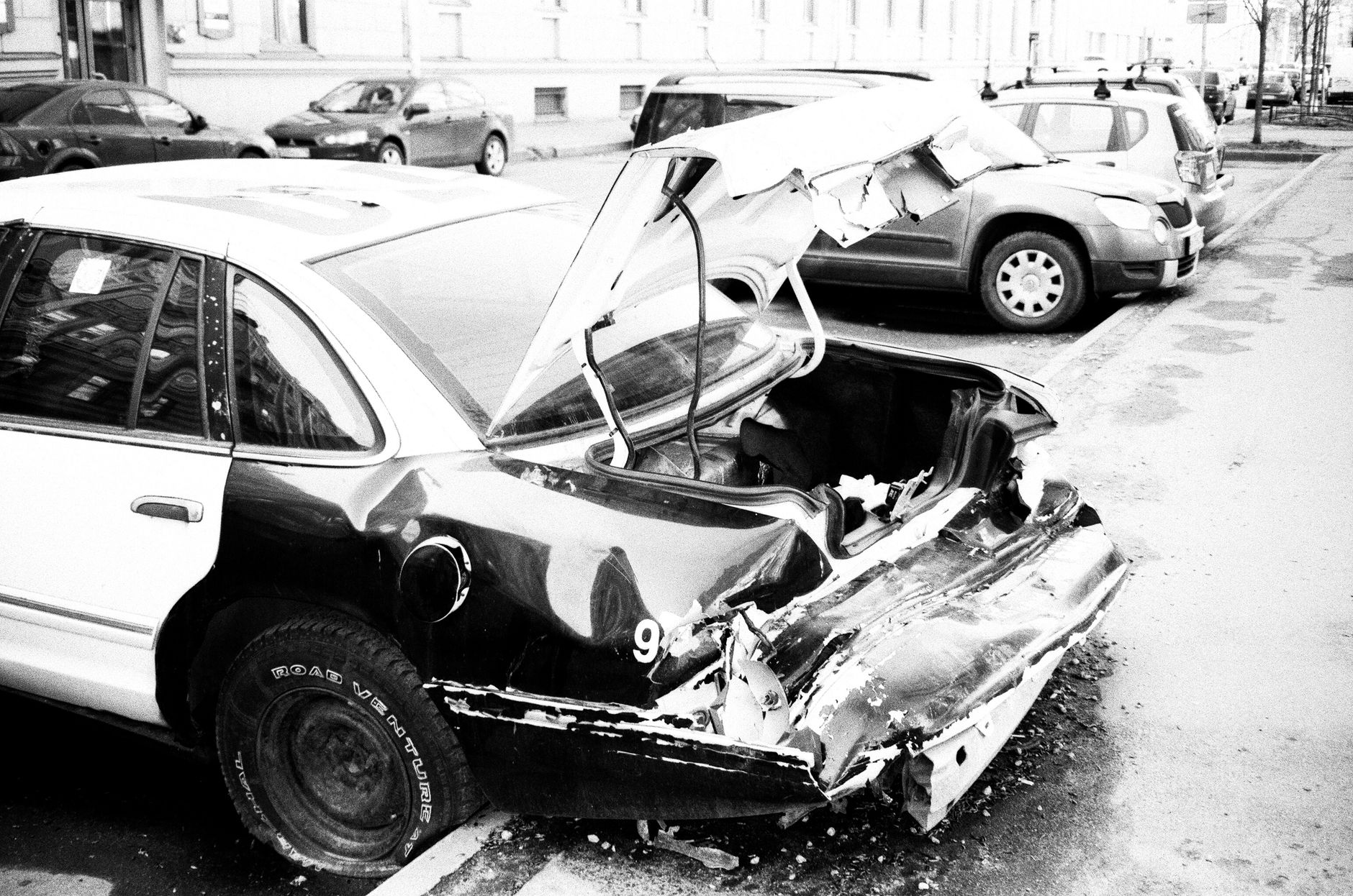 A damaged vehicle on a city street after a collision, in black and white